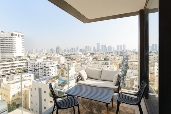 A balcony with a sofa and two chairs, overlooking a cityscape with multiple buildings.