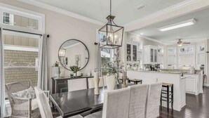 A modern kitchen with white cabinetry, a central island, and a dining area with a dark table and white chairs. - Private Pool-4 bikes (Santa Rosa Beach)