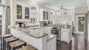 A kitchen with white cabinets, granite countertops, and a central island with stools. - Private Pool-4 bikes (Santa Rosa Beach)