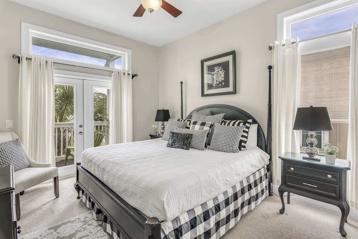A bedroom with a bed, a nightstand, a chair, a ceiling fan, and a window with curtains.