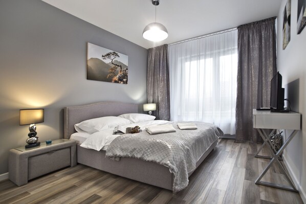Un dormitorio moderno con cama, lámparas de noche, televisión de pantalla plana y un cuadro en la pared.