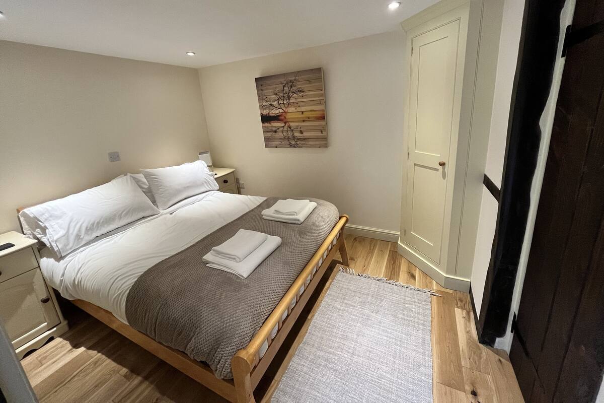 A bedroom with a bed, nightstands, a painting, and a door.