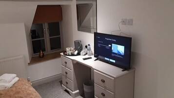 Un dormitorio con cama, escritorio con computadora, ventana con persiana y radiador.