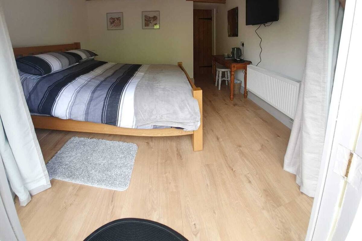 A bedroom with a wooden bed, a desk, a chair, a radiator, and a TV mounted on the wall.