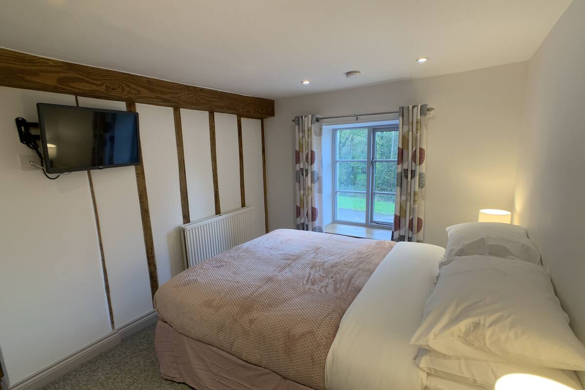 A bedroom with a bed, a TV mounted on the wall, a window with curtains, and a radiator.