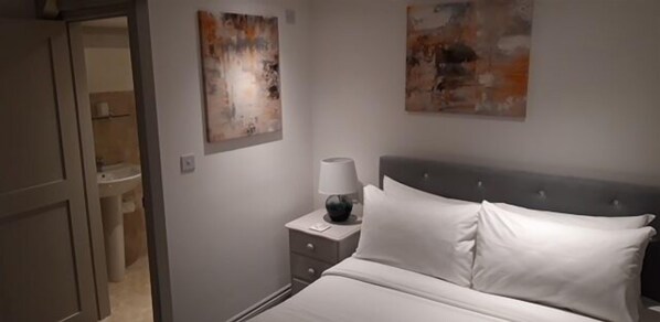 A bedroom with a bed, nightstand, lamp, and abstract wall art. - Swan House Tea Room Bed & Breakfast (Lydney)