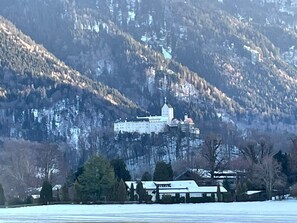Een kasteelachtig gebouw met een opvallende toren, omgeven door een besneeuwd landschap en beboste bergen.