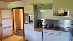 A compact kitchen with wooden cabinets, a built-in oven, a coffee maker, and a sink. - PrienZeit vacation apartment with fantastic panoramic views (Aschau)