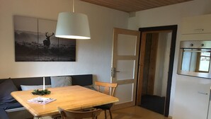 A cozy living area with a wooden dining table, two chairs, a sofa, and a large painting. A white pendant light hangs above the table. - PrienZeit vacation apartment with fantastic panoramic views (Aschau)
