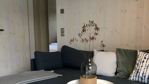 Een moderne woonkamer met een donkerblauwe hoekbank, een witte salontafel met glazen koepel en een grijze plaid.