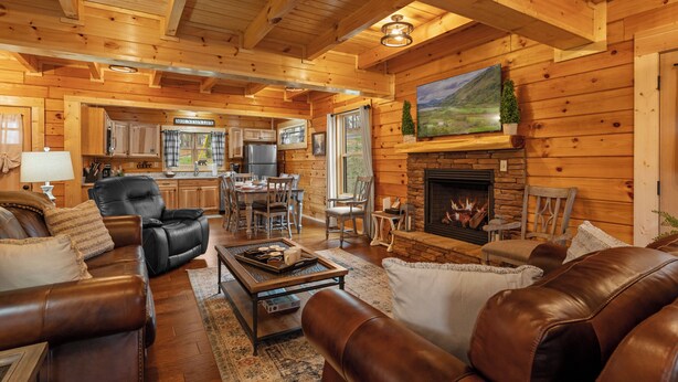 A cozy log cabin interior with a fireplace, leather sofas, a dining area, and a kitchen. - W/C Accessible, Private Log Cabin, with Mountain Views, Private Hot Tub (Sevierville)