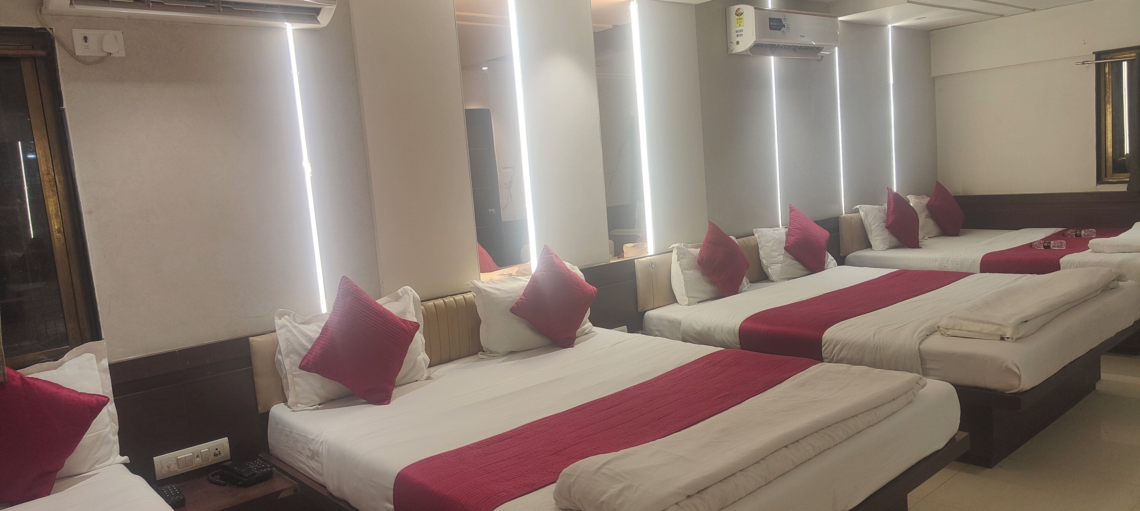 Habitación de hotel con cuatro camas dispuestas en fila, cada una con ropa blanca y detalles rojos.