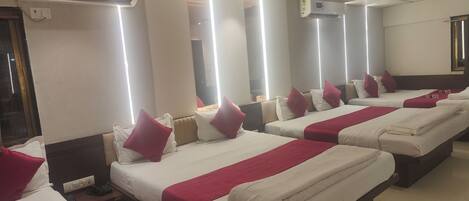 Habitación de hotel con cuatro camas dispuestas en fila, cada una con ropa blanca y detalles rojos.