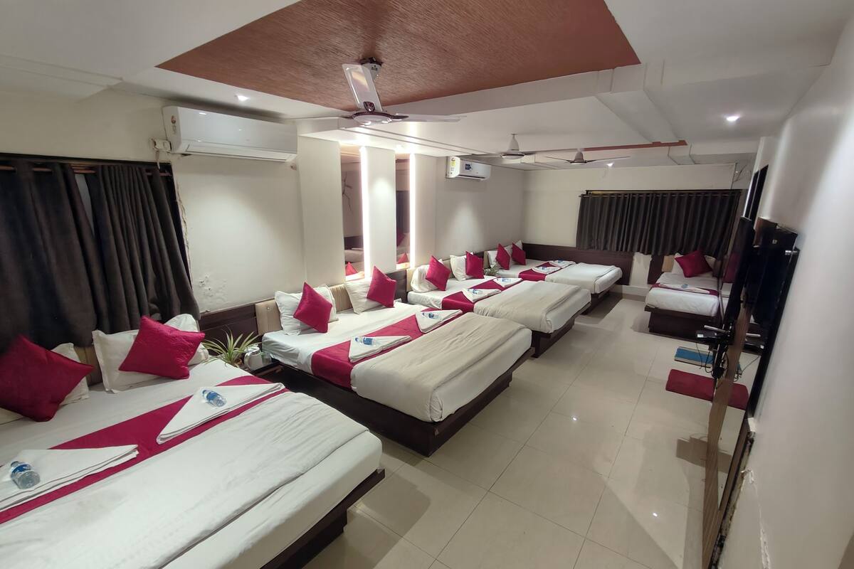 Una habitación de hotel con varias camas, unidades de aire acondicionado, ventiladores de techo y un televisor.
