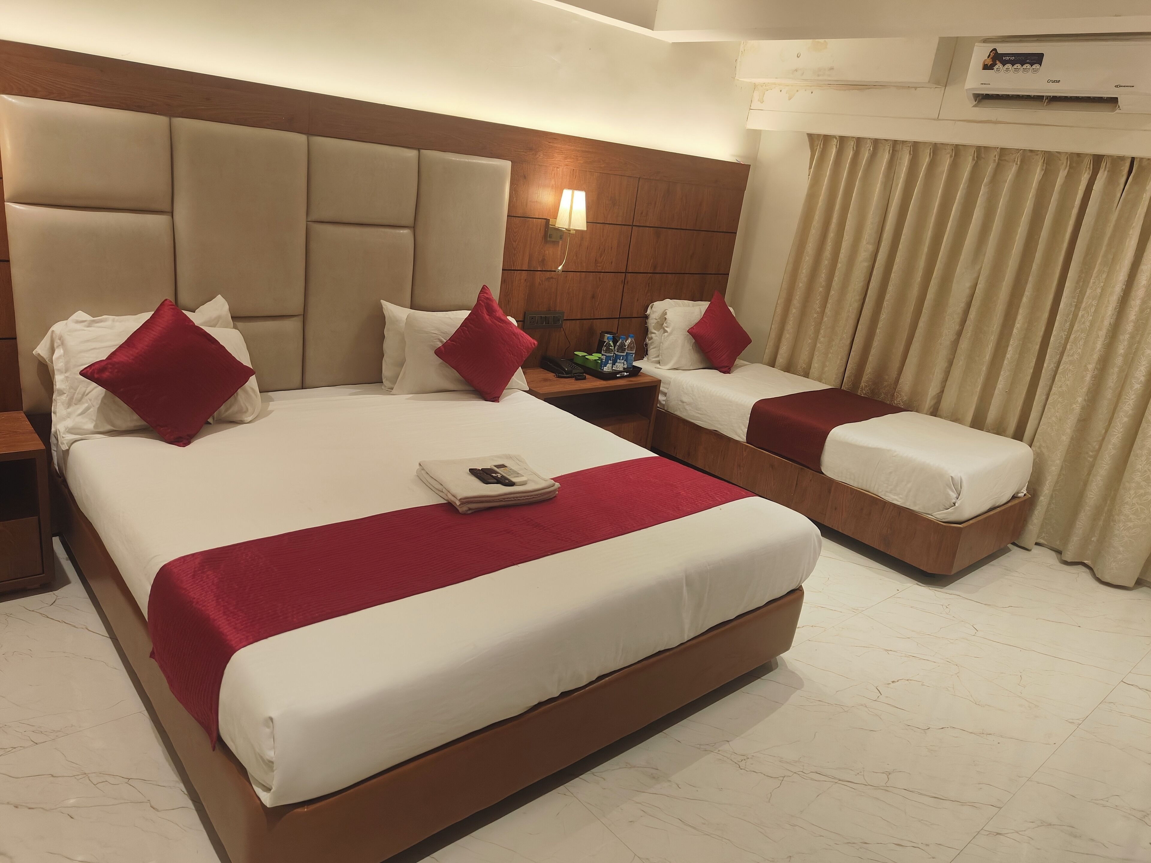 Een hotelkamer met een groot bed, twee kleinere bedden, een nachtkastje en een wandairconditioner.