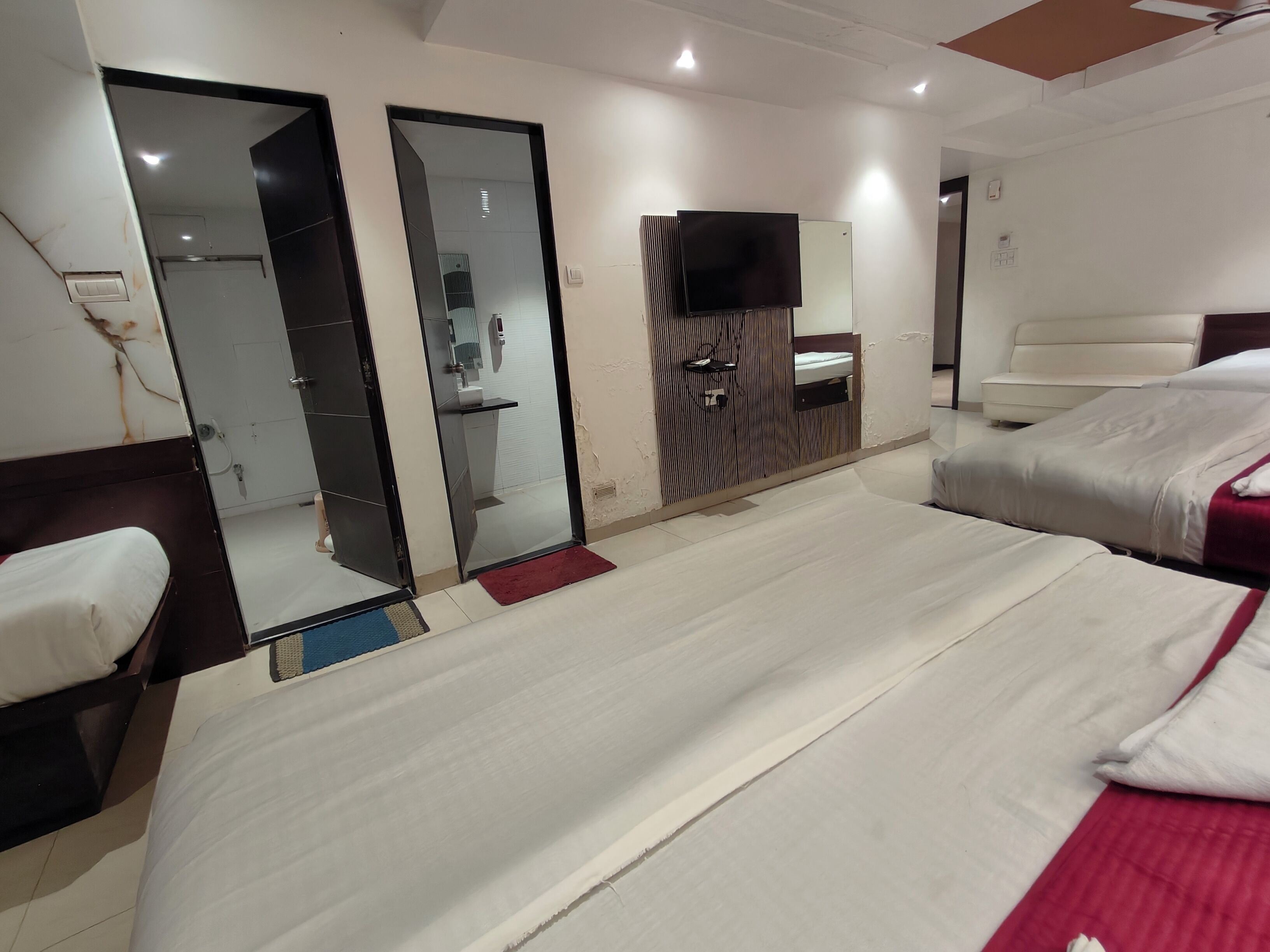 A hotel room with a large bed, a separate seating area, a mirror, a television, and a bathroom visible through an open door.