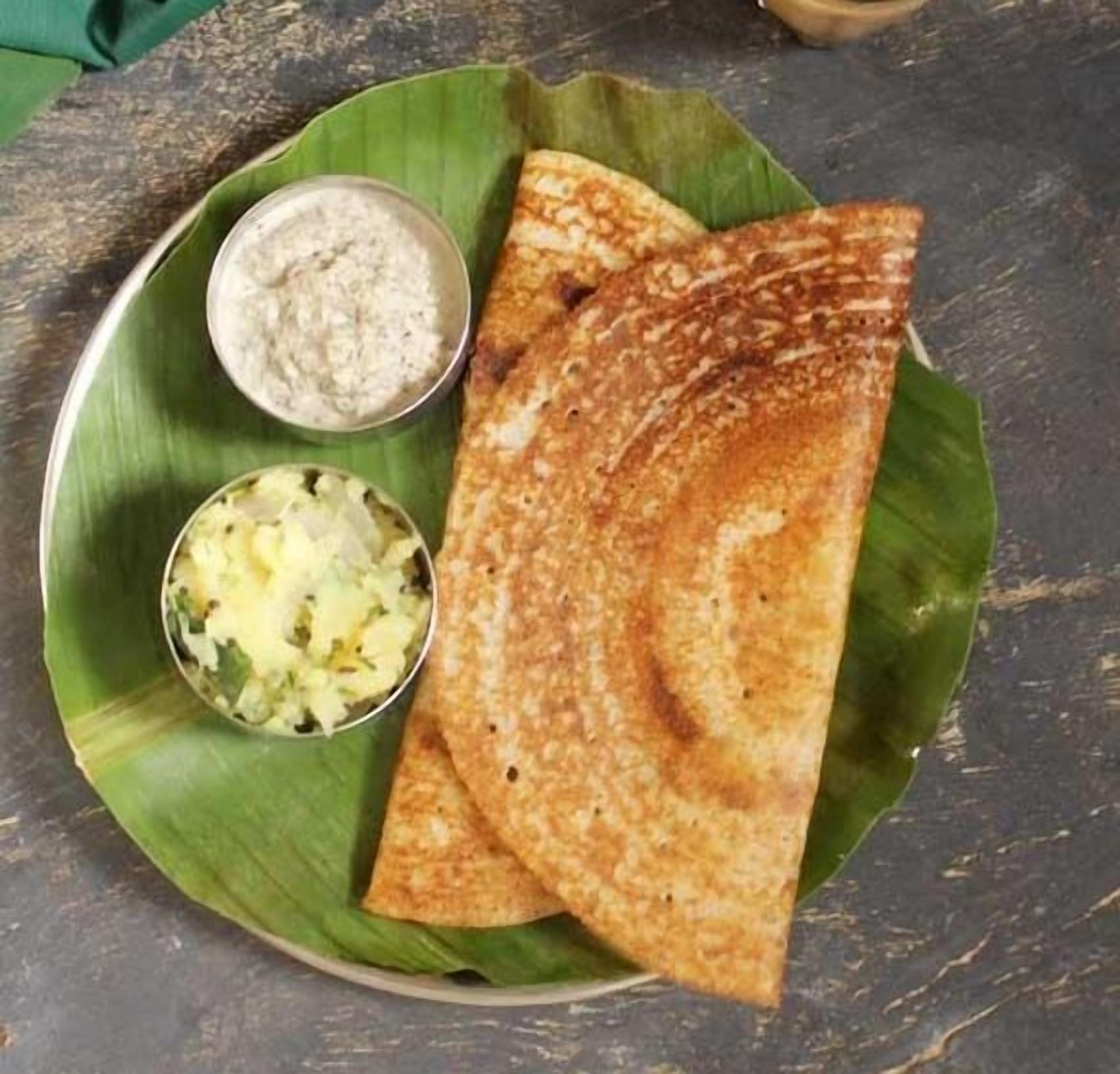 A plate with two dosas and two chutneys on a banana leaf.