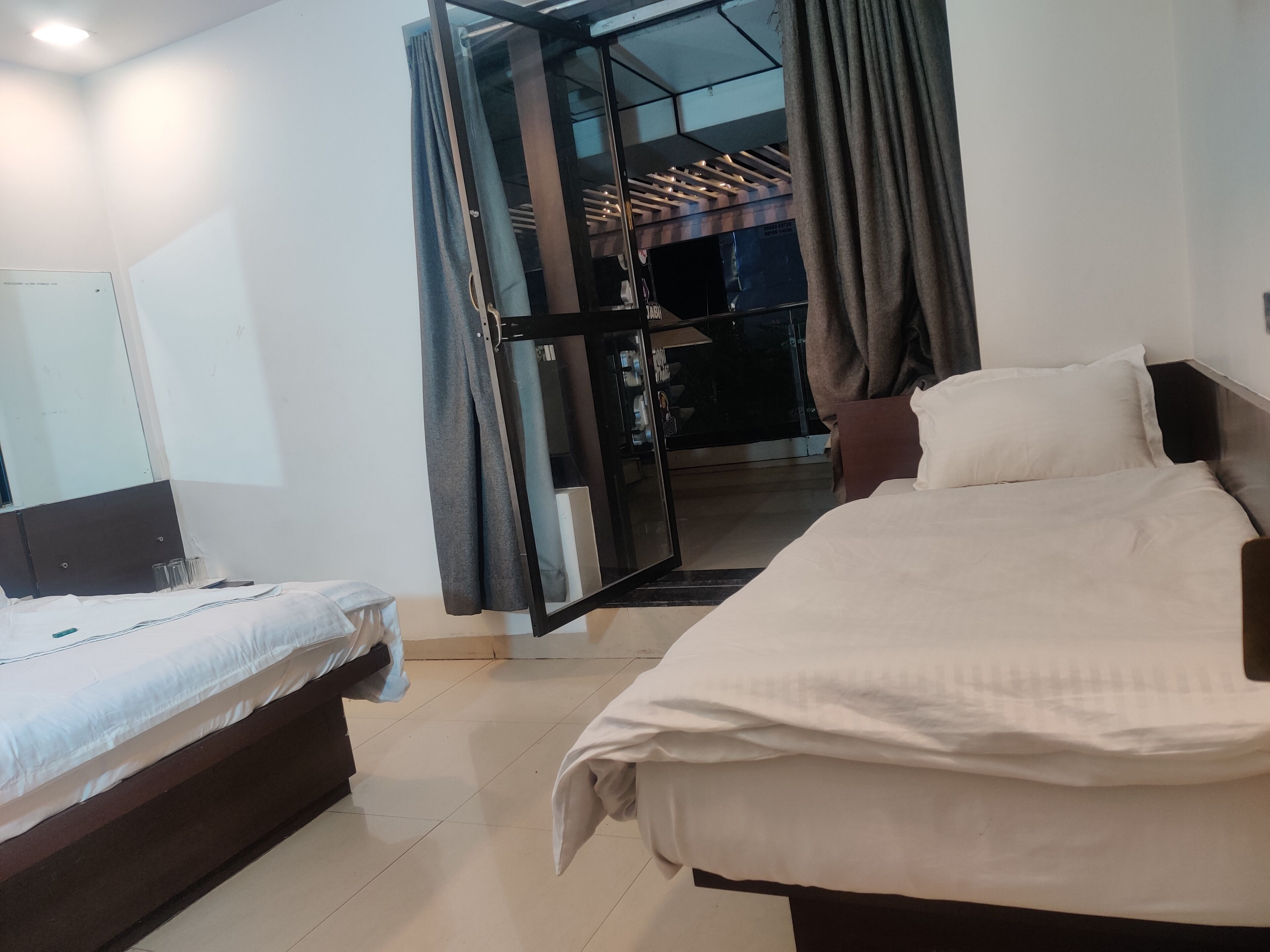 A hotel room with two beds, a large mirror, and a sliding glass door leading to a balcony.