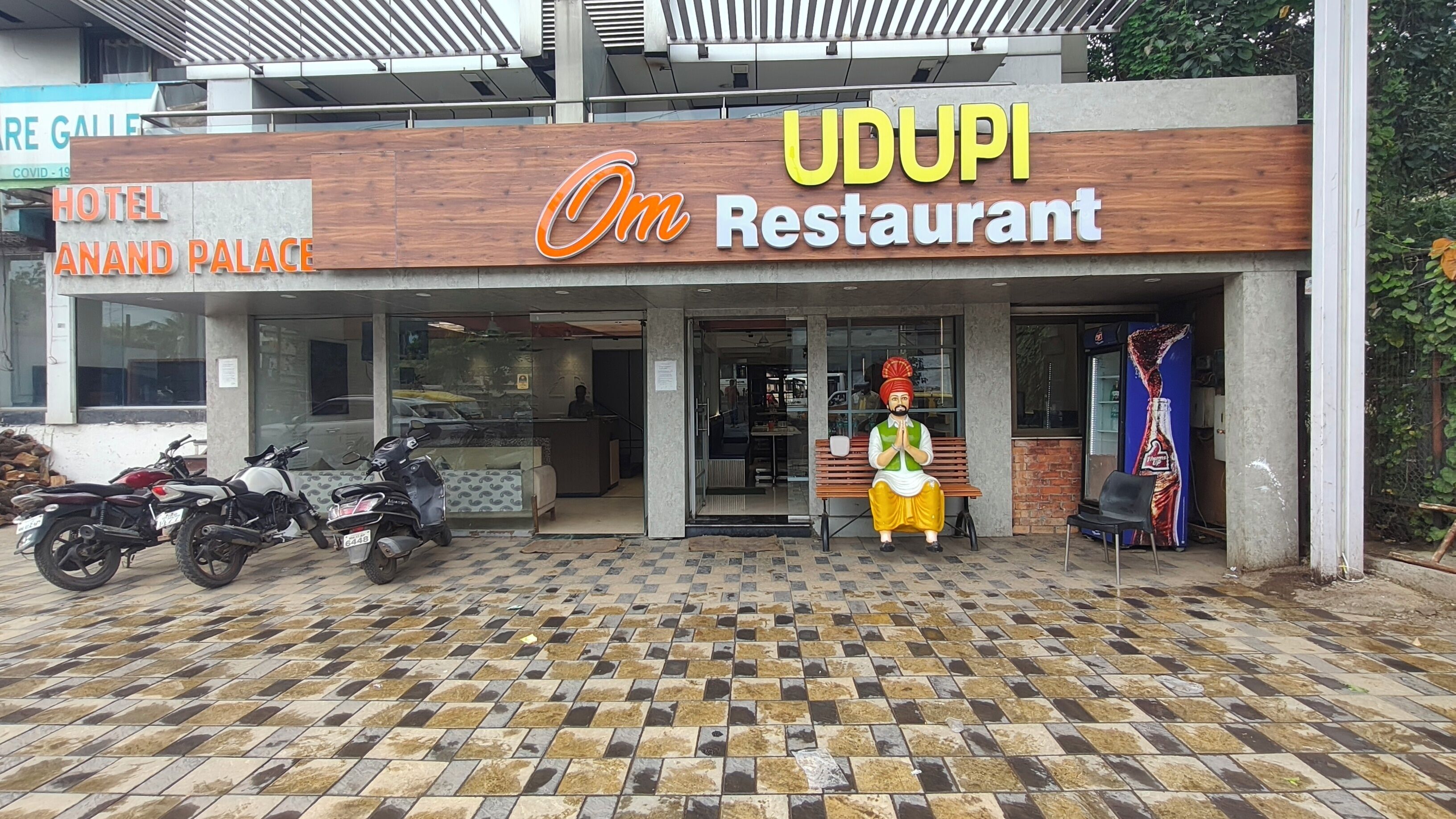 A hotel and restaurant named UDUPI with a tiled entrance and a statue of a man in traditional attire outside.