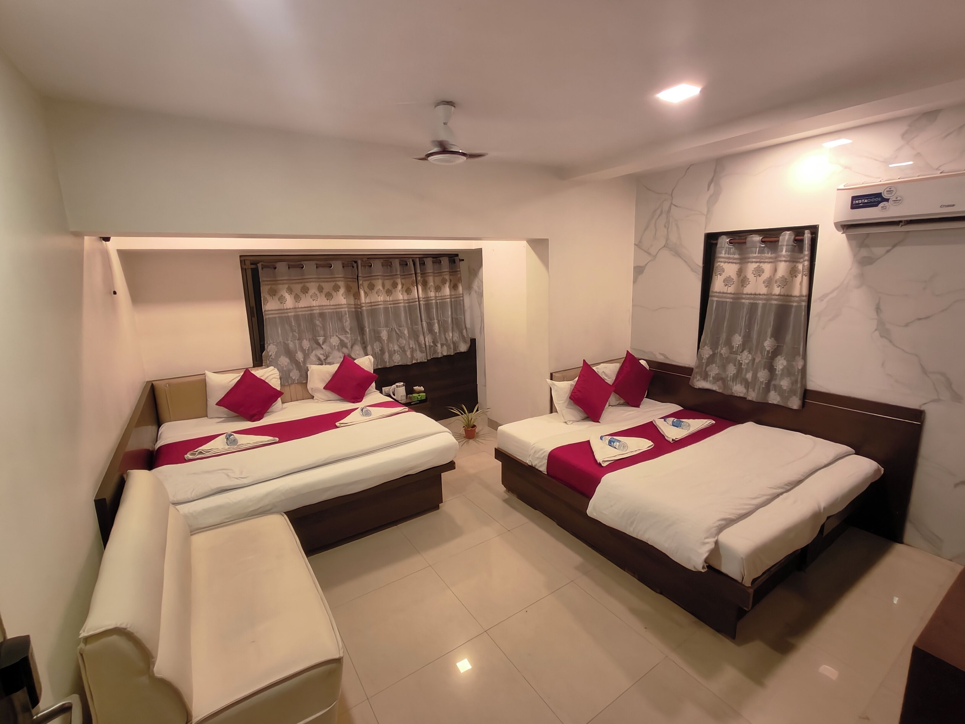 A hotel room with two beds, a ceiling fan, a marble wall, and an air conditioning unit.