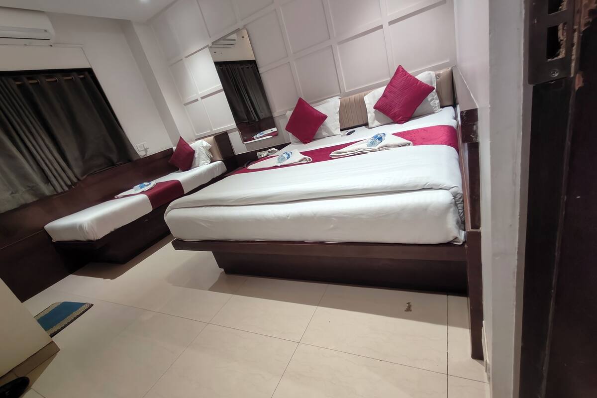 Habitación de hotel con una cama grande, una cama más pequeña y un sofá. Hay un espejo en la pared, una ventana con cortinas y una puerta.