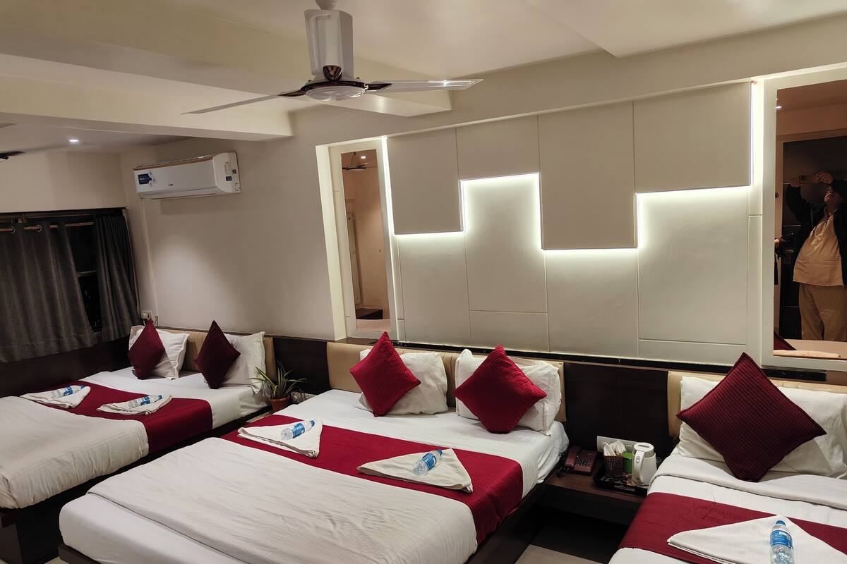 Habitación de hotel con cuatro camas, ventilador de techo, espejo grande y minibar.