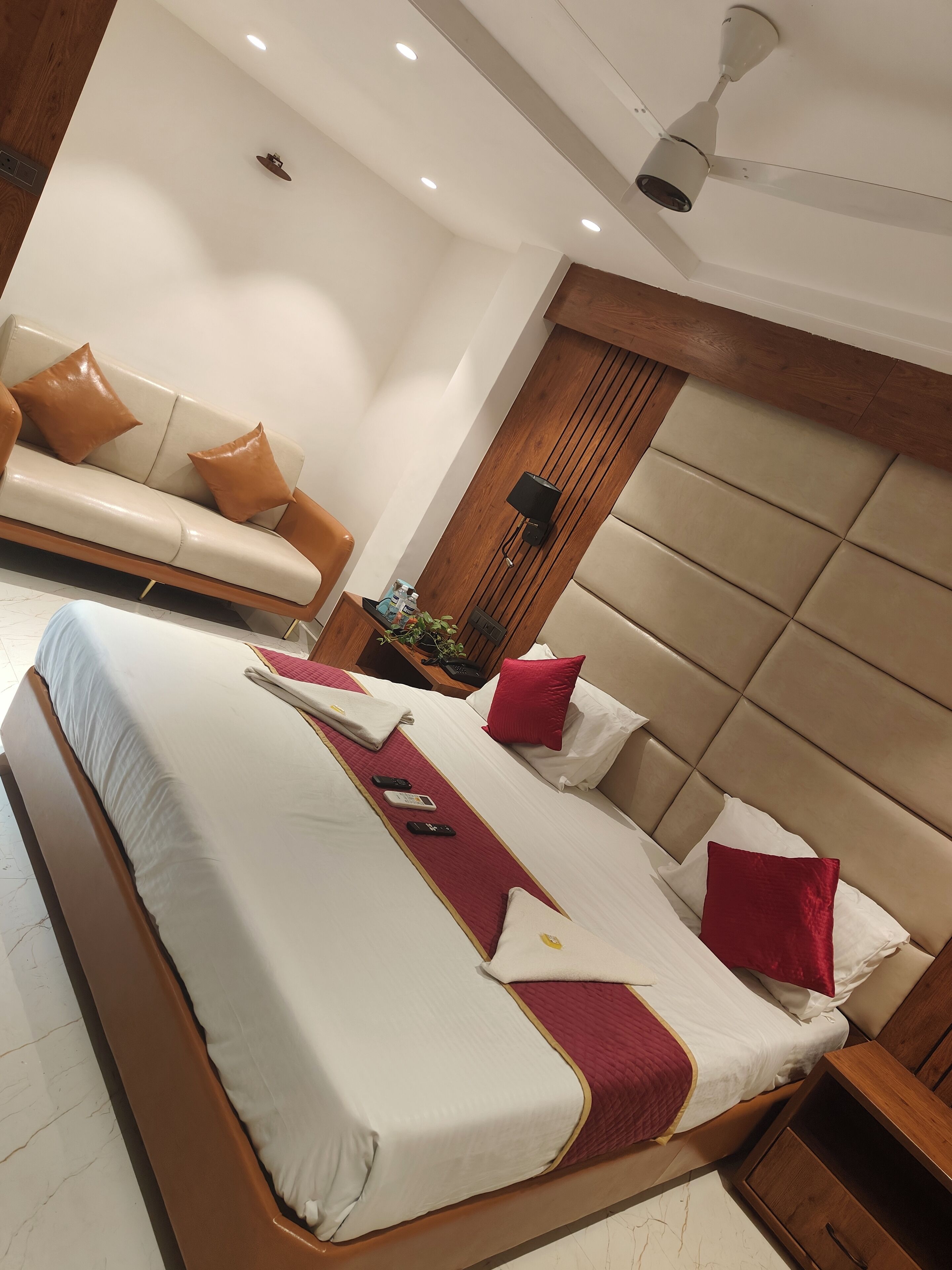 A hotel room with a large bed, a sofa, a wooden headboard, and a ceiling fan.