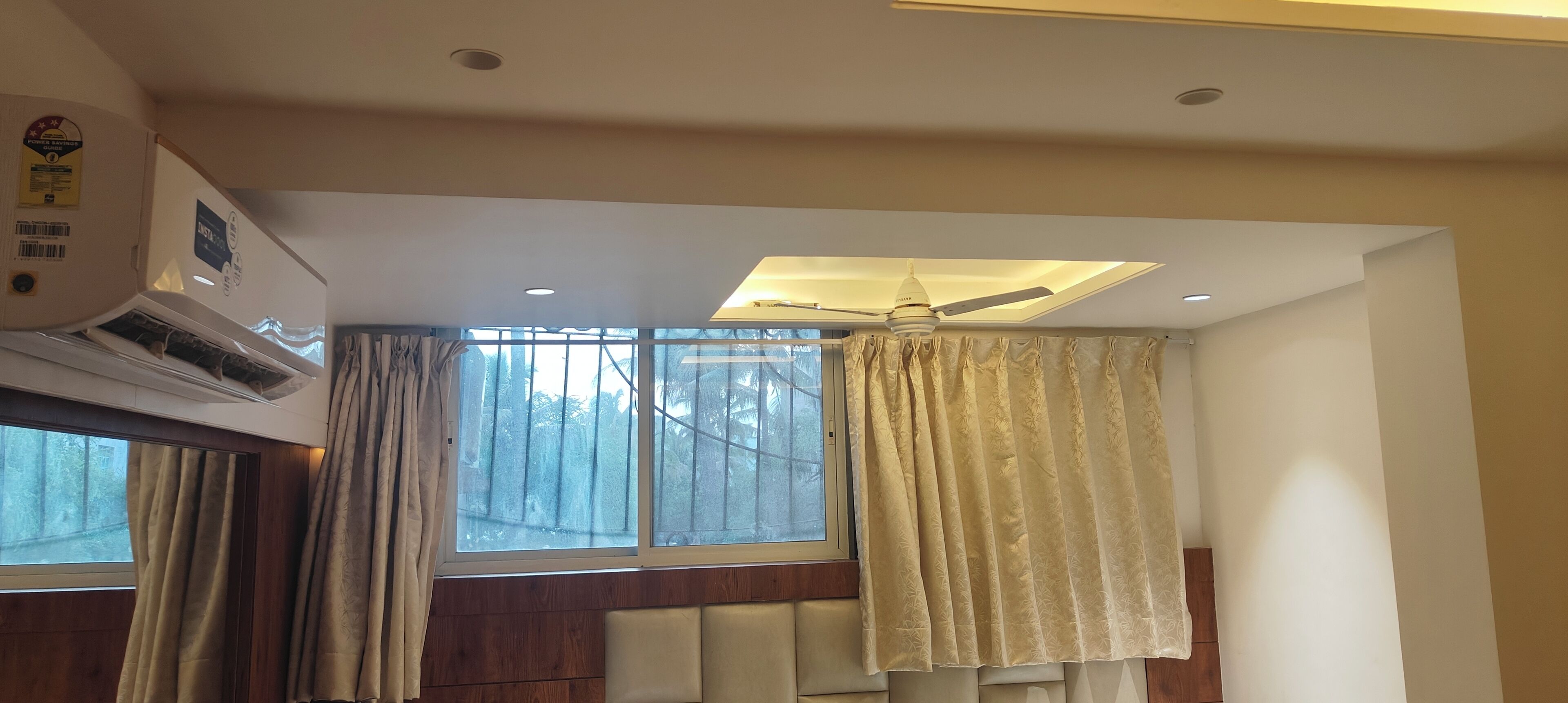 Une pièce dotée d’un ventilateur de plafond, de grandes fenêtres avec des rideaux et d’un appareil de climatisation.