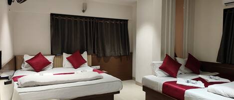 Habitación de hotel con dos camas, cada una con sábanas blancas y almohadas rojas, un ventilador de techo y un equipo de aire acondicionado.