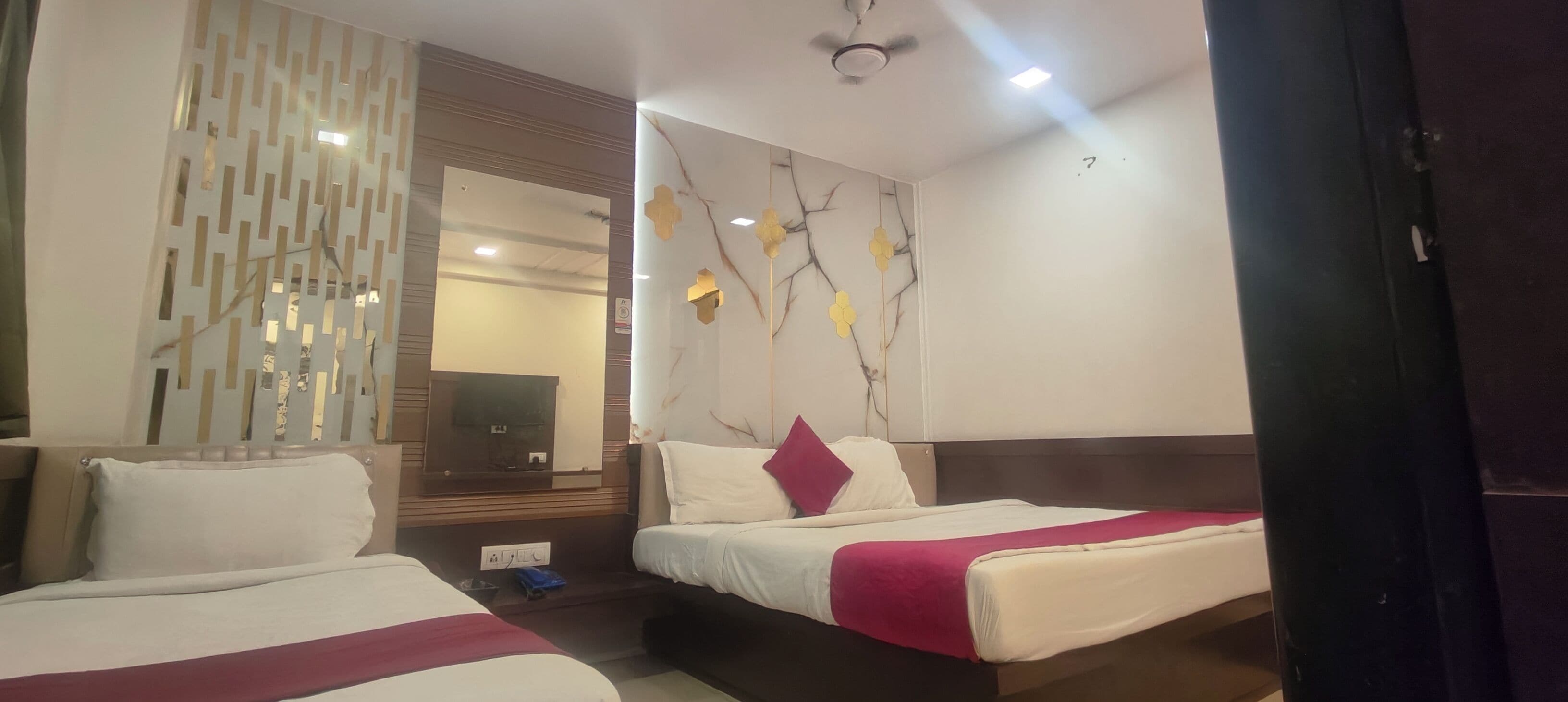 A hotel room with two beds, a decorative wall, a ceiling fan, and a mirror.
