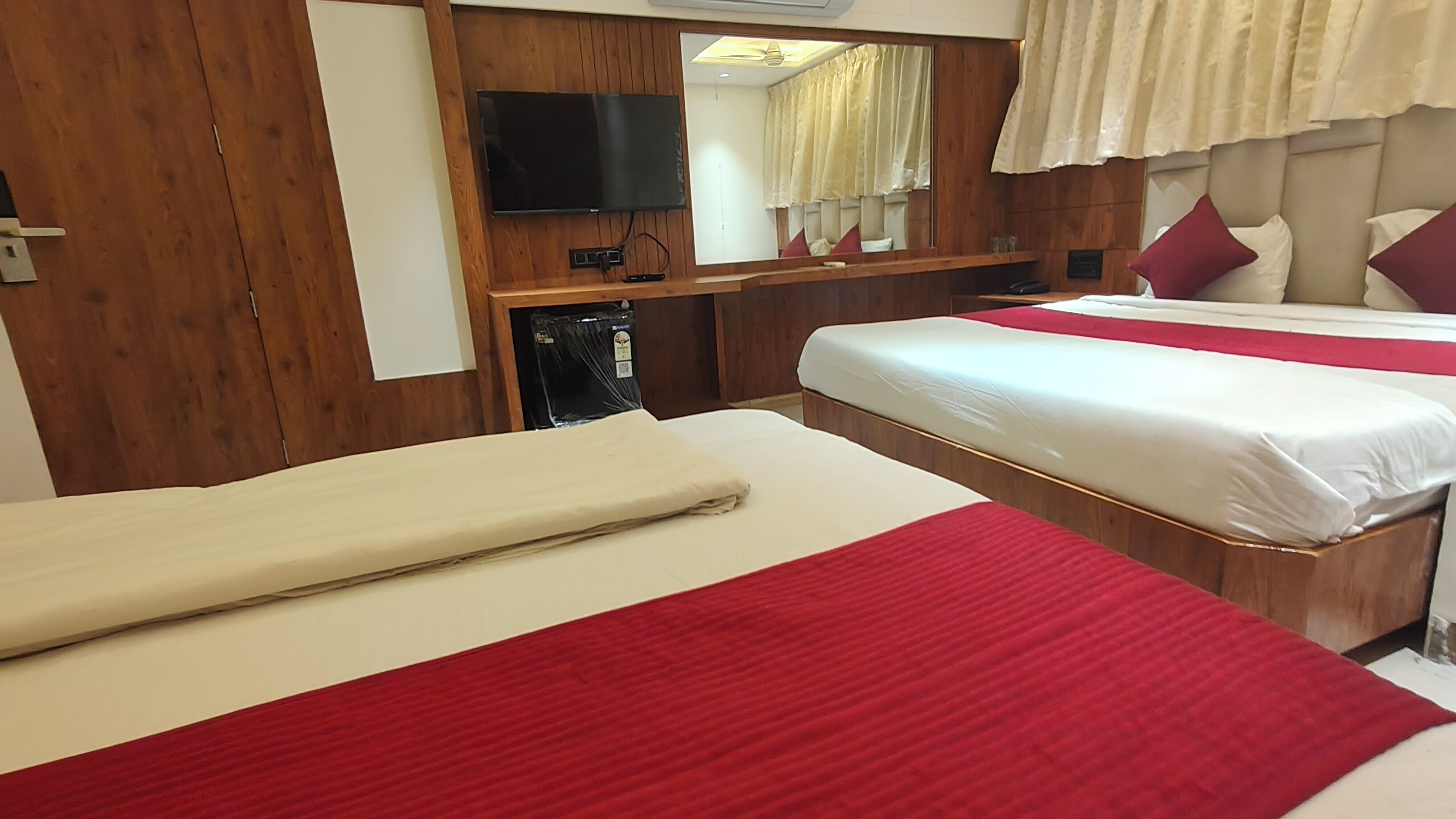 A hotel room with two beds, a television, a mirror, and a wooden panel wall.
