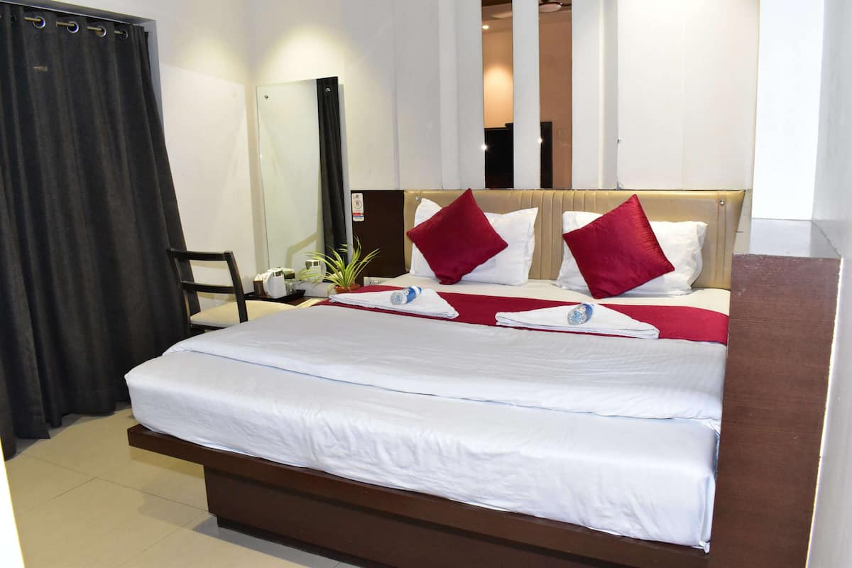 A neatly made bed with white linens and red pillows, a wooden headboard, a bedside table with a lamp, and a chair.