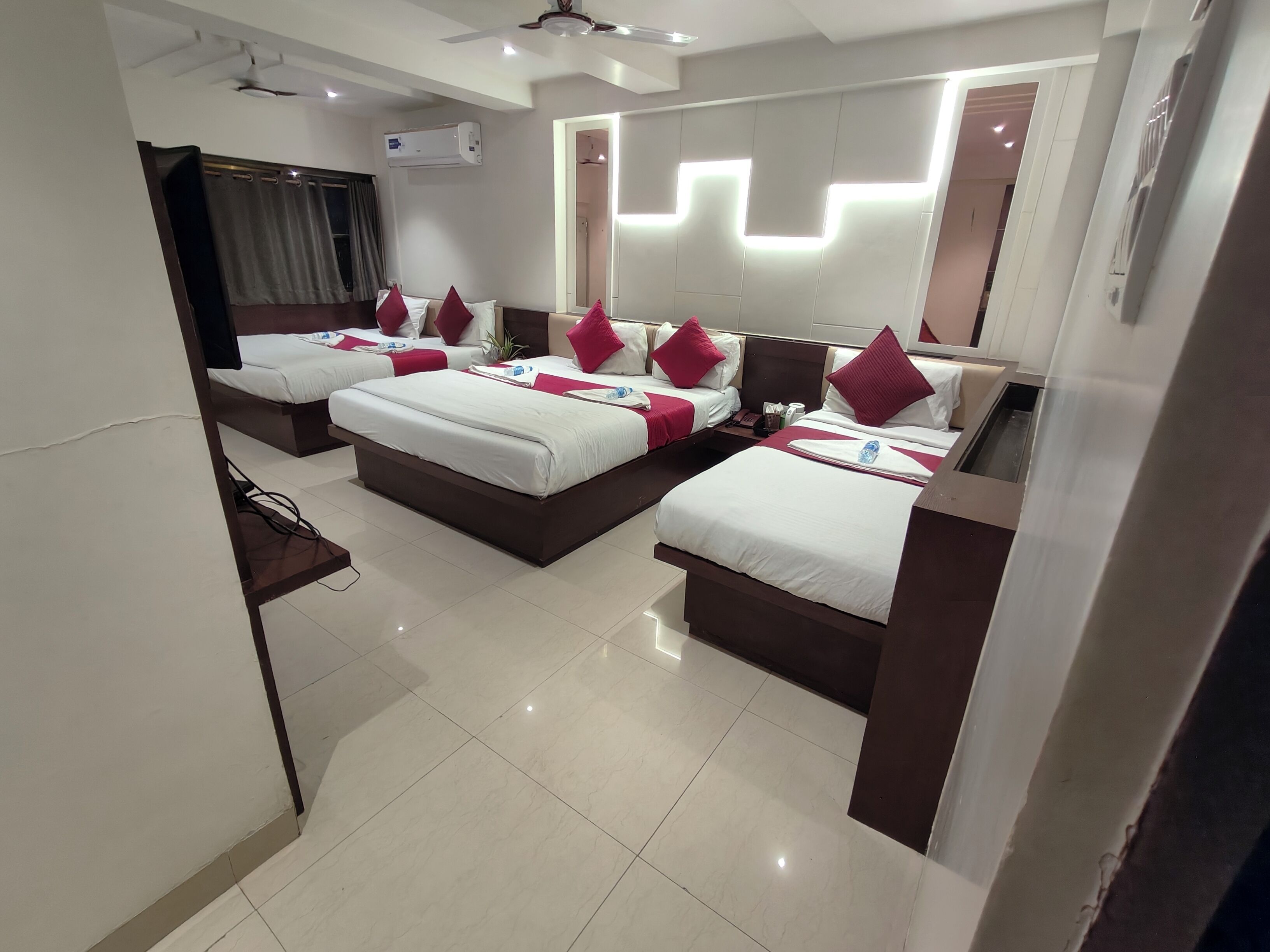 A hotel room with three beds, a ceiling fan, an air conditioning unit, and a modern light fixture.