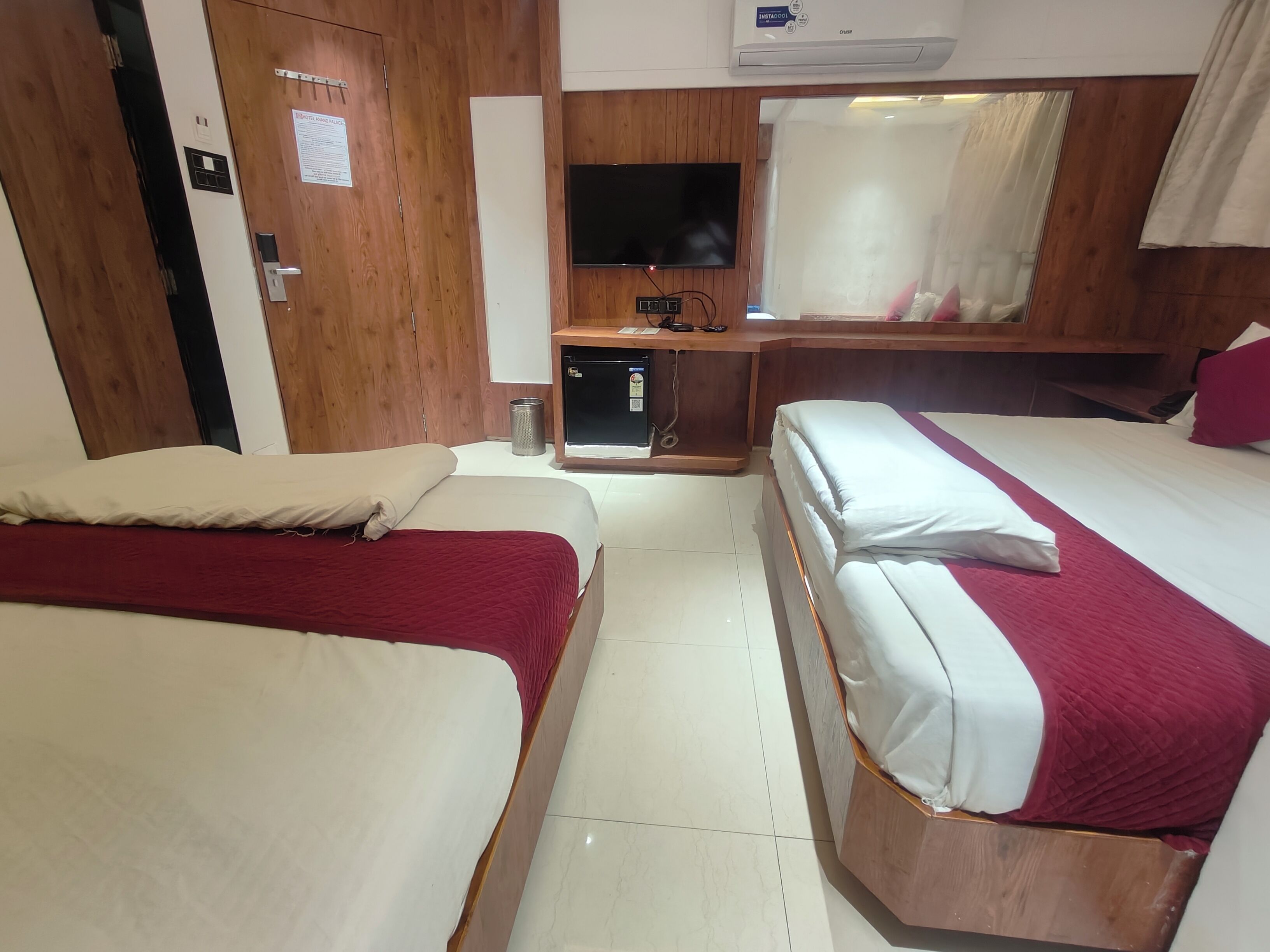 Habitación de hotel con dos camas, televisión, escritorio pequeño y espejo.