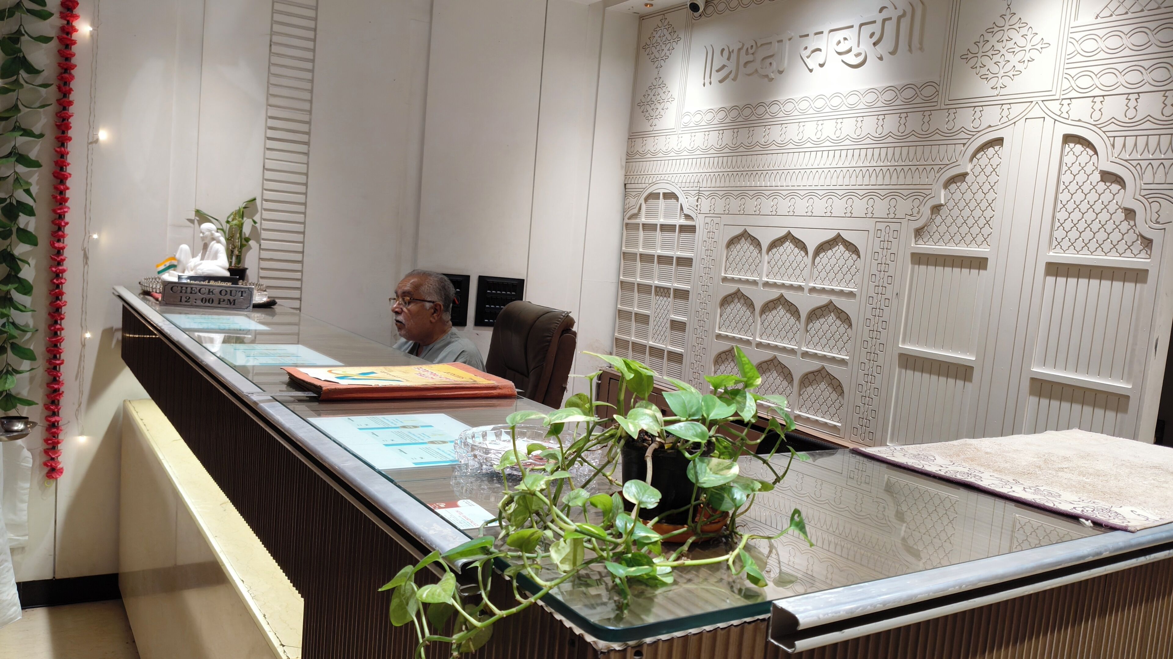 A reception desk with a glass top, a potted plant, and a sign indicating check-out time.