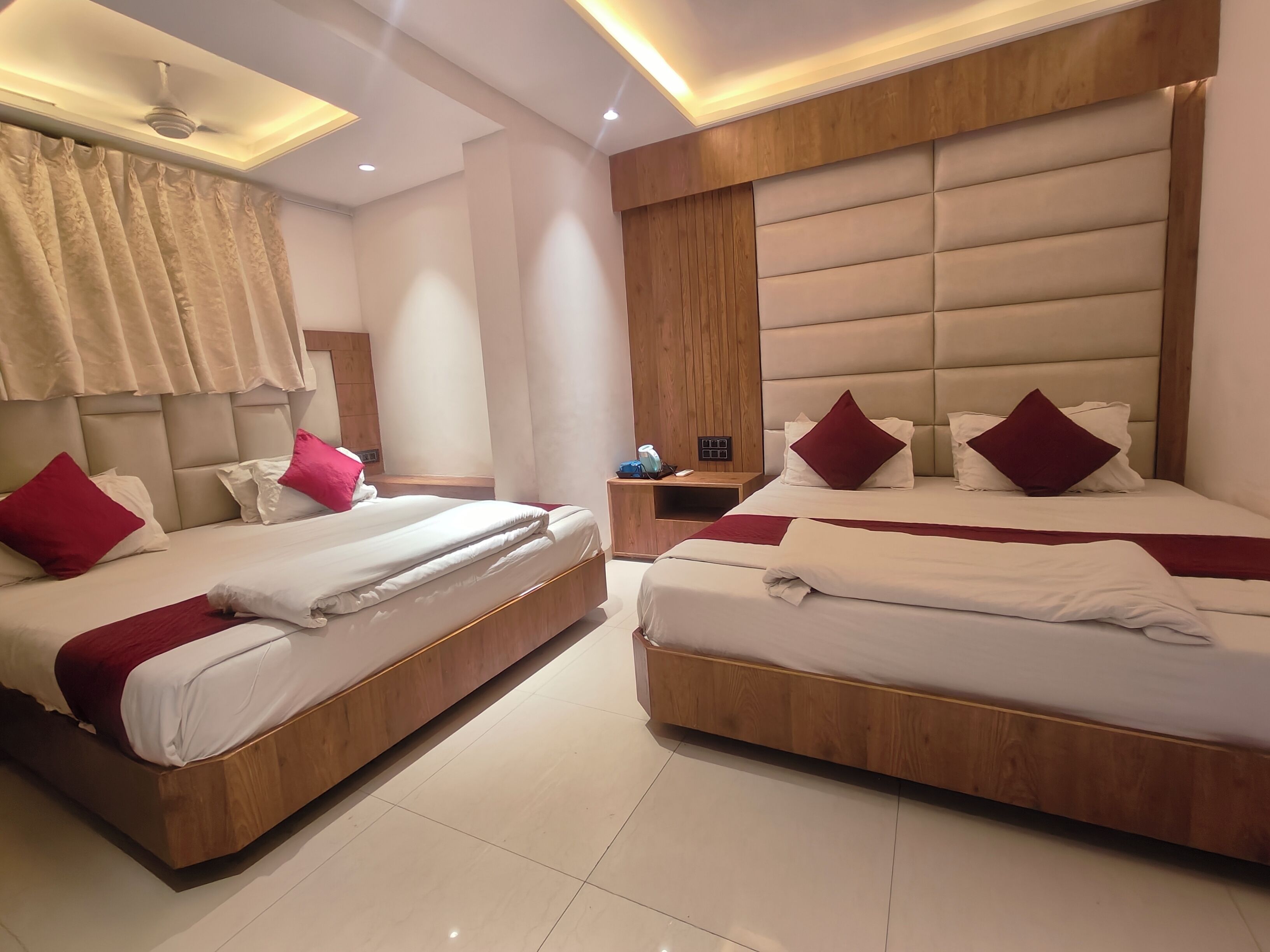 Habitación de hotel con dos camas, cabecera de madera, mesita de noche y ventilador de techo.