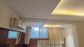 Une chambre moderne dotée d’un ventilateur de plafond, d’un appareil de climatisation, de grandes fenêtres avec rideaux et d’un mur revêtu de panneaux en bois.