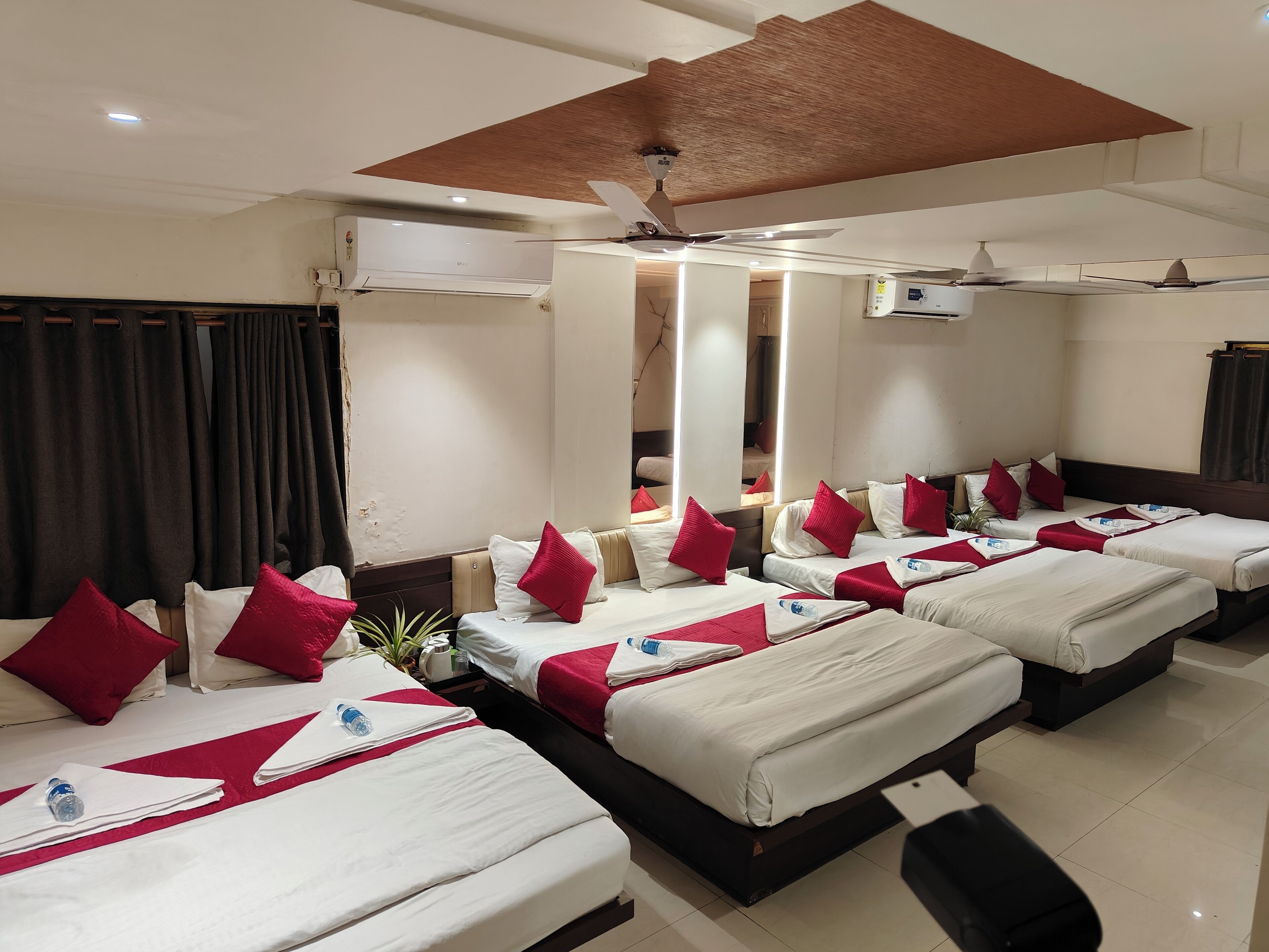 Une chambre d’hôtel dotée de plusieurs lits, chacun avec une literie rouge et blanche, un ventilateur de plafond et un appareil de climatisation.