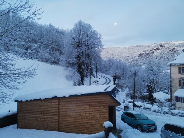 A snow-covered landscape with a wooden cabin, a winding road, and a car parked in front.
