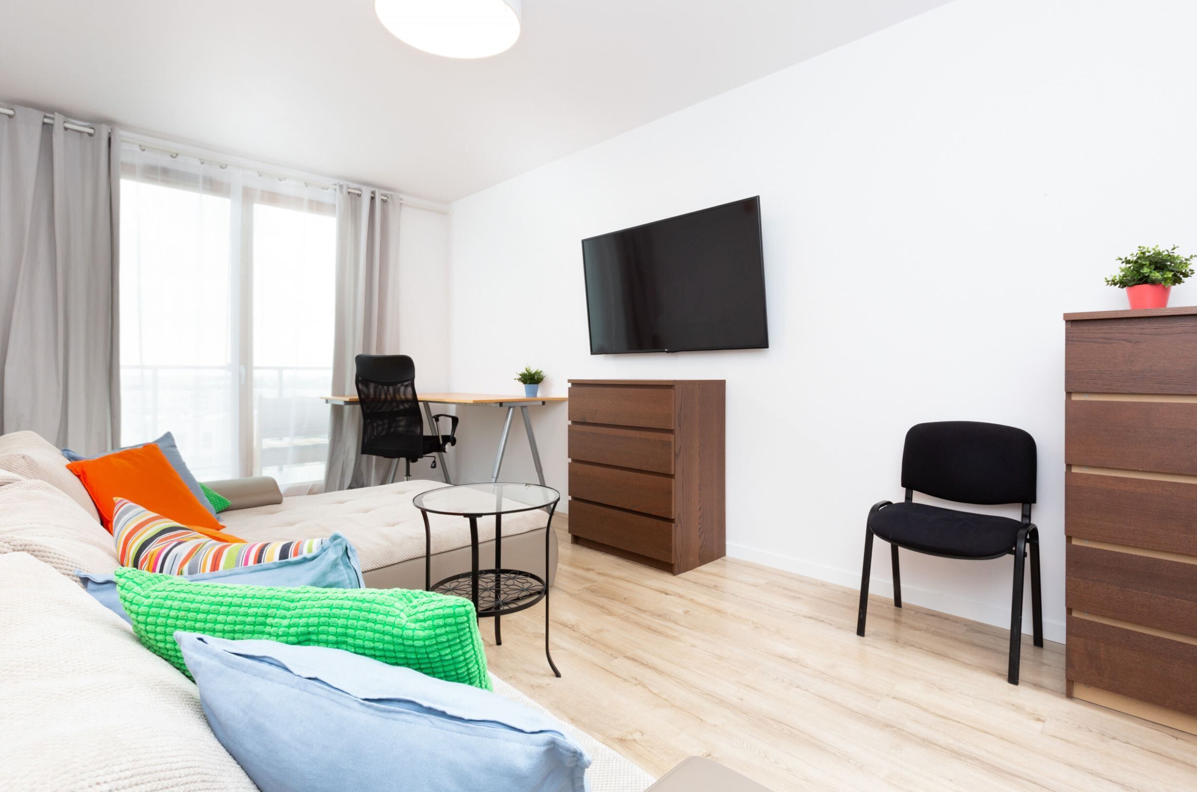 Un dormitorio moderno con una cama, un escritorio, una silla, un televisor y un armario.