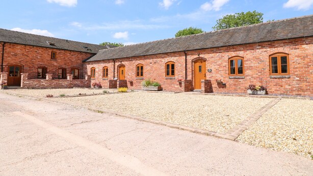A brick building with multiple arched windows and doors, a gravel courtyard, and a clear sky. - Pipistrelle (Stoke-on-Trent)