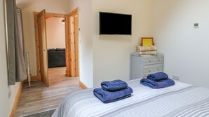 A bedroom with a bed, a TV, a dresser, and a wooden door leading to another room. - Pipistrelle (Stoke-on-Trent)