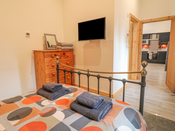A bedroom with a bed, a wooden dresser, a television, and a view into the kitchen. - Pipistrelle (Stoke-on-Trent)