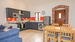 A modern kitchen with grey cabinets, a built-in oven, and a washing machine. There is a dining area with a wooden table and chairs. - Pipistrelle (Stoke-on-Trent)