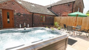 A hot tub in a backyard with a brick house, a wooden door, and a patio with chairs and an umbrella. - Pipistrelle (Stoke-on-Trent)
