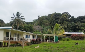 A two-story house with a covered porch and a small garden area. - "Jolly Rooster" Farm Cottage near famous Muri Beach  (Matavera)