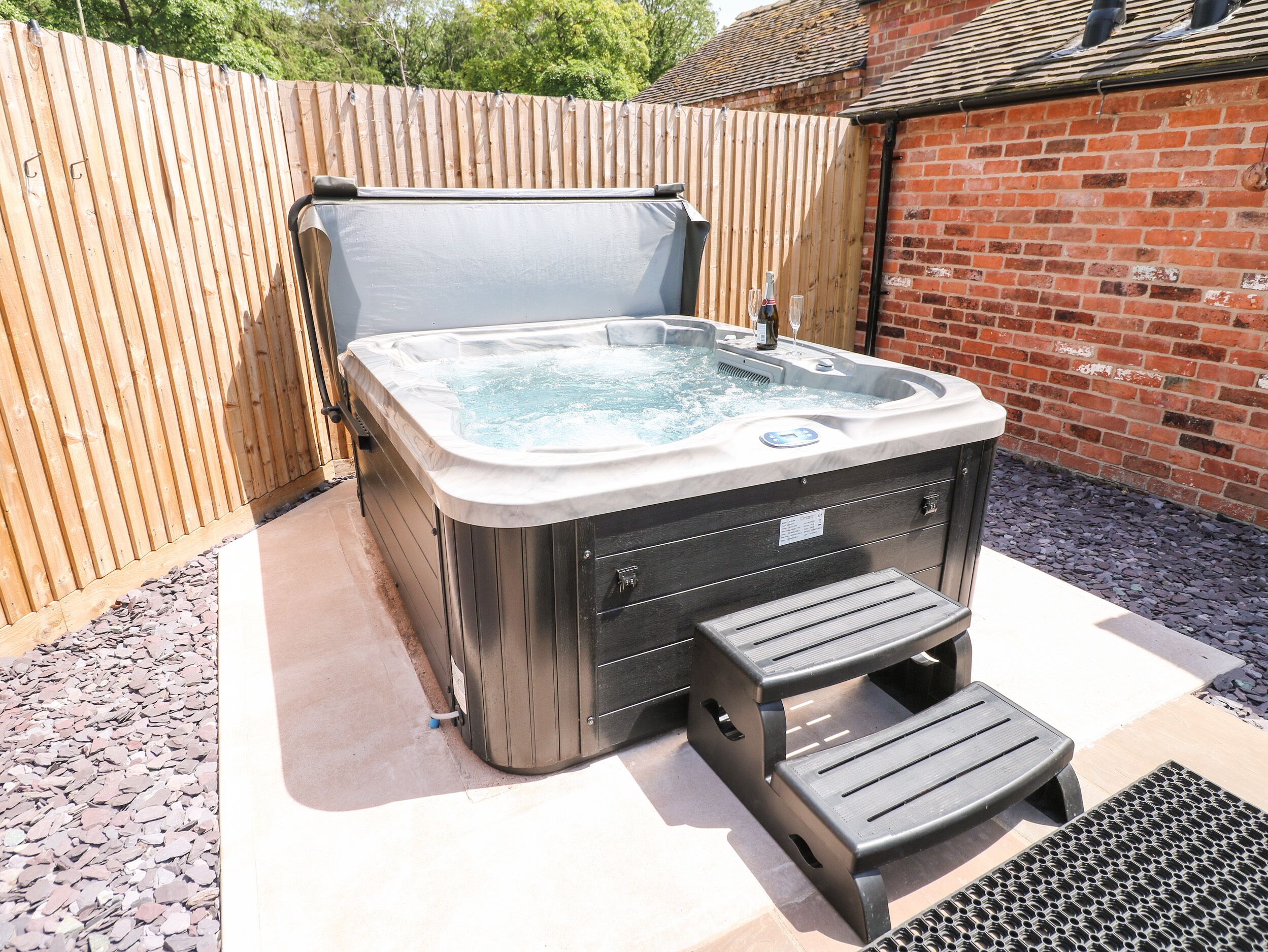 A hot tub with a built-in seat and steps, surrounded by a wooden fence and a brick wall.
