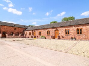 En murstensbygning med flere buede vinduer og døre, en grusgård og en klar blå himmel.