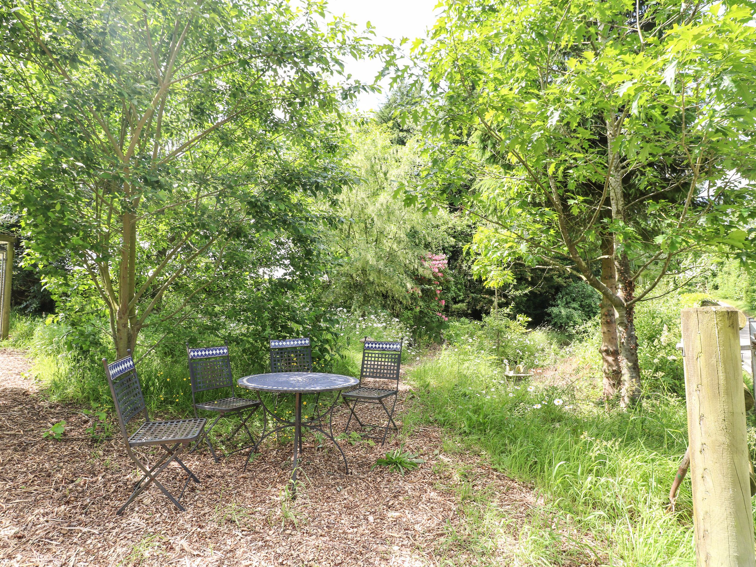 Een buitenzitplaats met metalen stoelen en een ronde tafel, omringd door bomen en begroeiing.