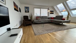Ein modernes Wohnzimmer mit einem Ecksofa, einem Liegestuhl, einem Couchtisch und einem Flachbildfernseher.